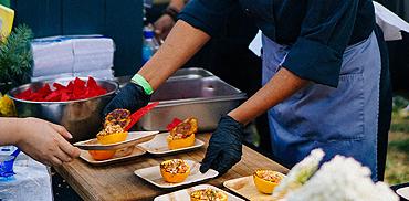 A photo of event staff serving food at an outdoor event.