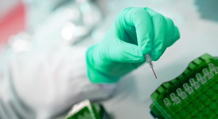 A lab worker wears green gloves