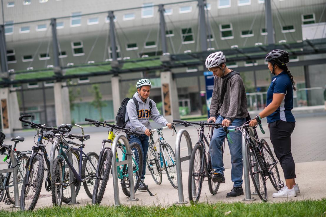 Three people locking their bikes at a bike rack outside the UBC Aquatic Centre.