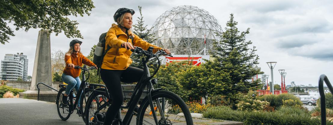 Two people riding their Zygg e-bikes on the Seawall bike path in front of Science World.