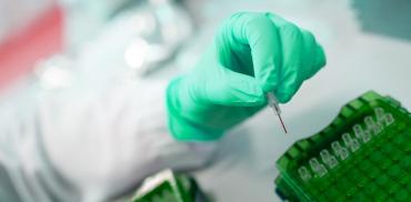 A lab worker wears green gloves