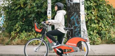 A person on an orange Mobi bike share waits at a traffic stop.