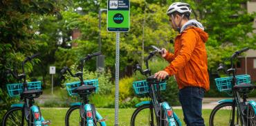 A person checks out a HOPR bike through their phone while standing in front of a row of HOPR bikes.