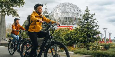 Two people riding their Zygg e-bikes on the Seawall bike path in front of Science World.